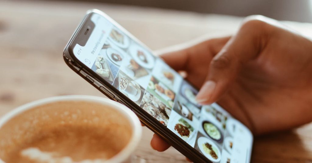Hand browsing social media photos on a smartphone next to a cup of coffee indoors.